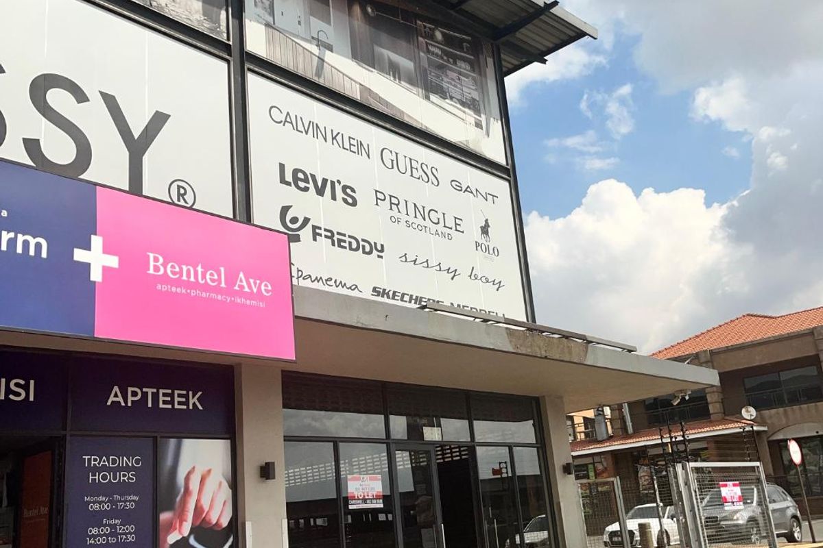 Front elevation of a retail commercial property featuring large glass storefront windows, metal awning, and prominent signage space in a well-maintained shopping center.