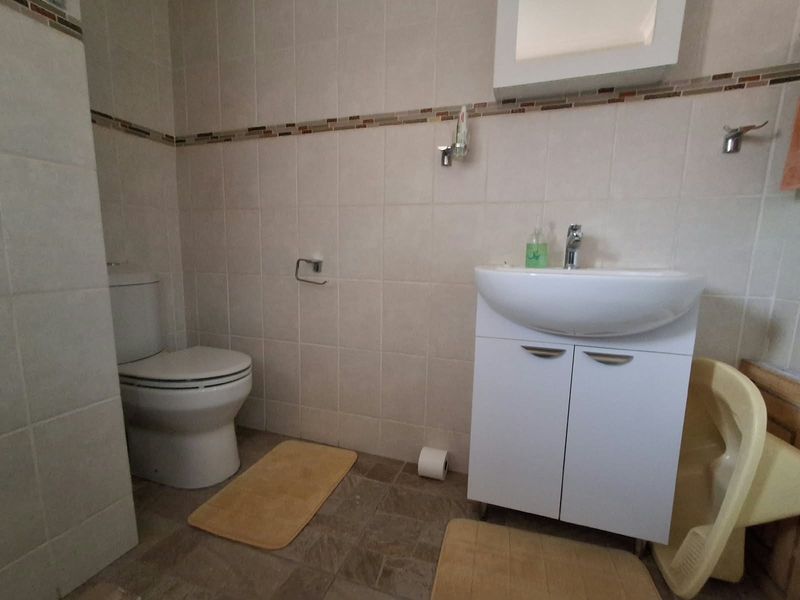 A functional bathroom featuring a white vanity cabinet with a basin, a toilet, and neutral wall tiling with a decorative border.