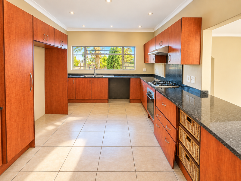 A functional kitchen featuring cherry-wood cabinetry, dark laminate countertops, a gas cooktop, and integrated oven, finished with neutral ceramic floor tiles.