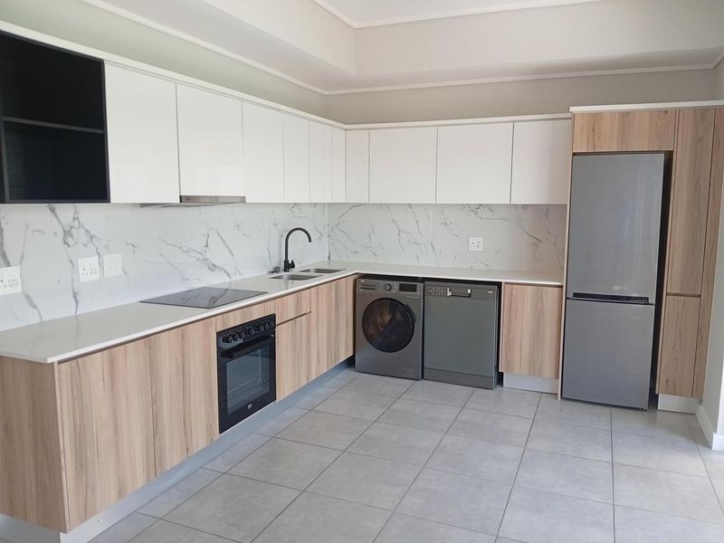 Modern kitchen featuring sleek white and wood-grain cabinetry, marble-look splashback, integrated oven, electric hob, and high-quality tiled flooring.
