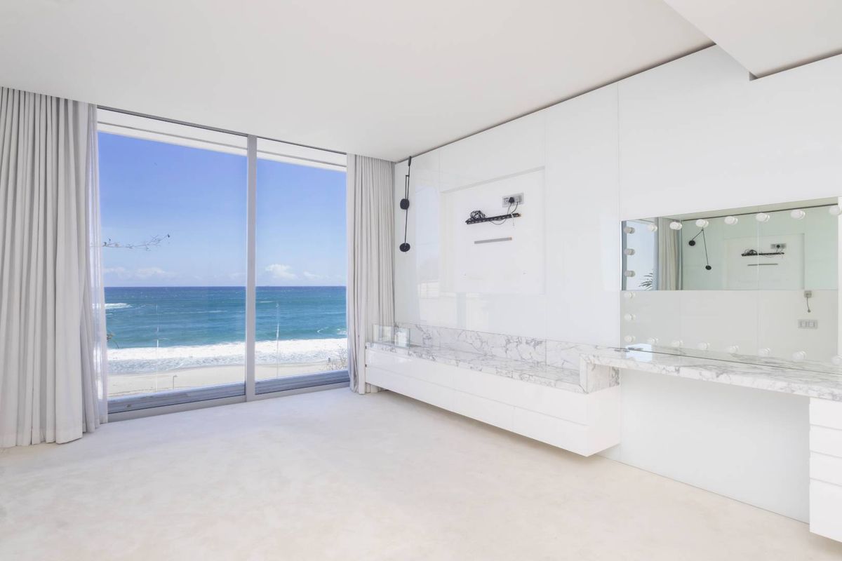 Spacious bedroom featuring floor-to-ceiling windows with panoramic ocean views, sleek built-in cabinetry, and a luxurious marble-topped vanity area.