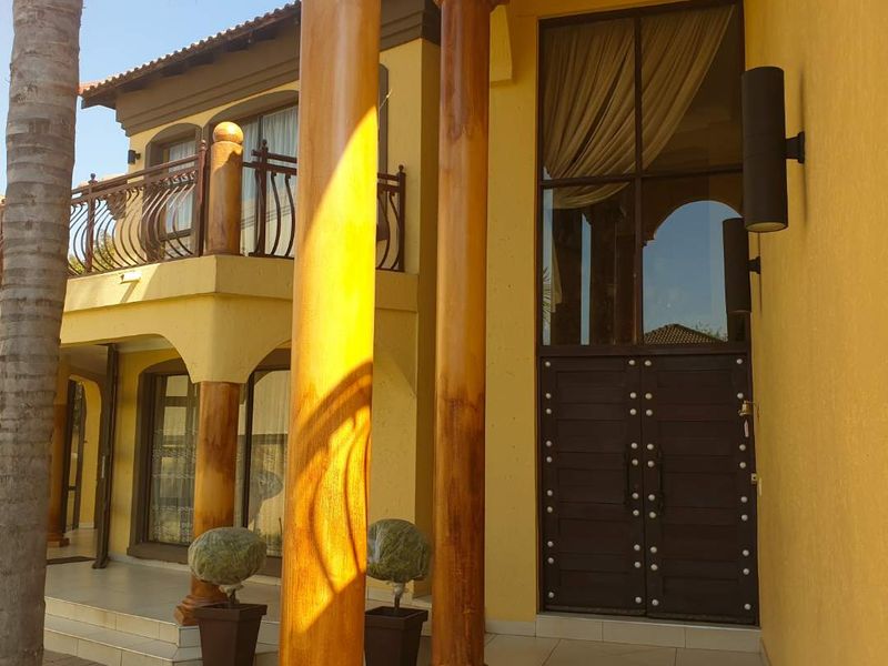 A grand entrance featuring decorative columns, a large double door with glass transom, and a tiled porch area leading to the main residence.