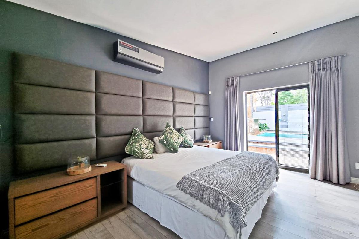 Spacious bedroom featuring modern upholstered wall paneling, a split-system air conditioner, and direct access to the outdoor pool area via sliding glass doors.
