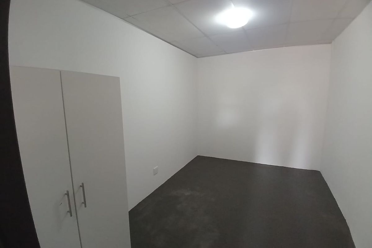 A simple, empty bedroom featuring plain white walls, dark flooring, and a built-in wardrobe, offering a blank canvas for personalization.