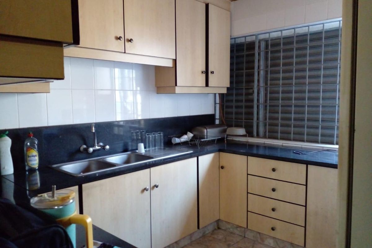A functional kitchen featuring light wood-tone cabinetry, black granite countertops, a double stainless steel sink, and a tiled backsplash with security bars on the window.
