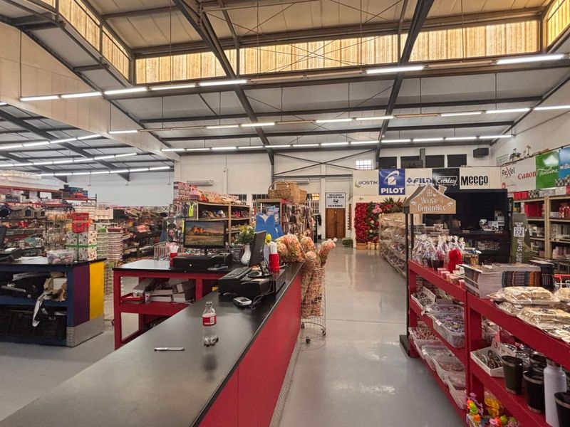Spacious retail interior featuring high exposed steel roof trusses, industrial lighting, polished concrete floors, and a central service counter area.
