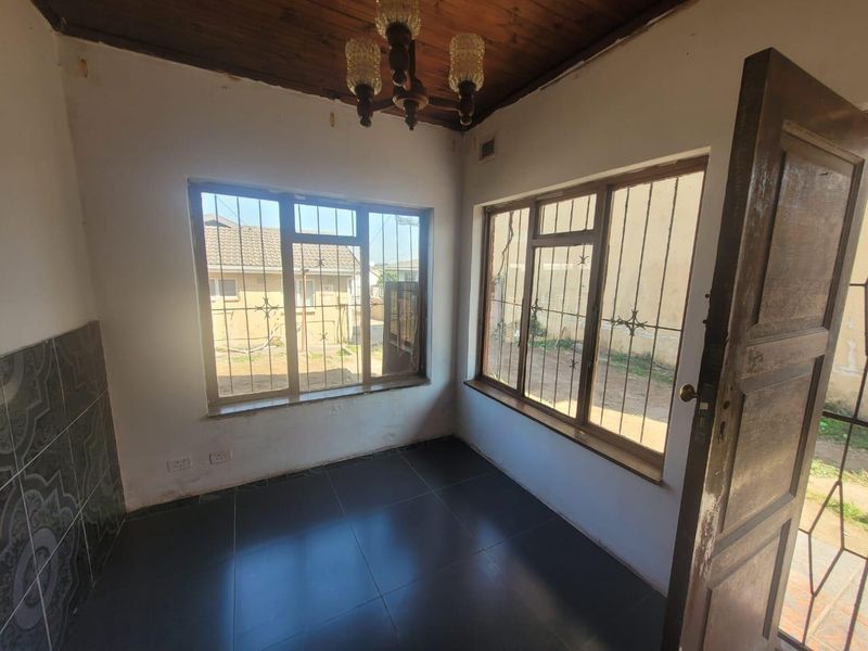 An empty living area featuring dark tiled floors, a timber ceiling, and large windows fitted with security bars.