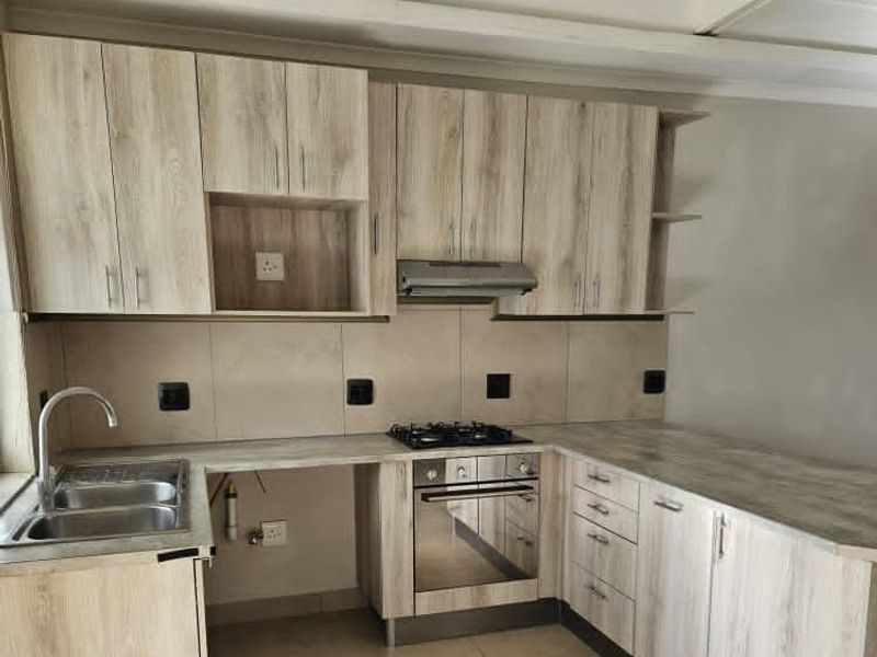 Modern kitchen featuring light wood-look cabinetry, laminate countertops, built-in oven, gas hob, and stainless steel sink with tiled splashback.