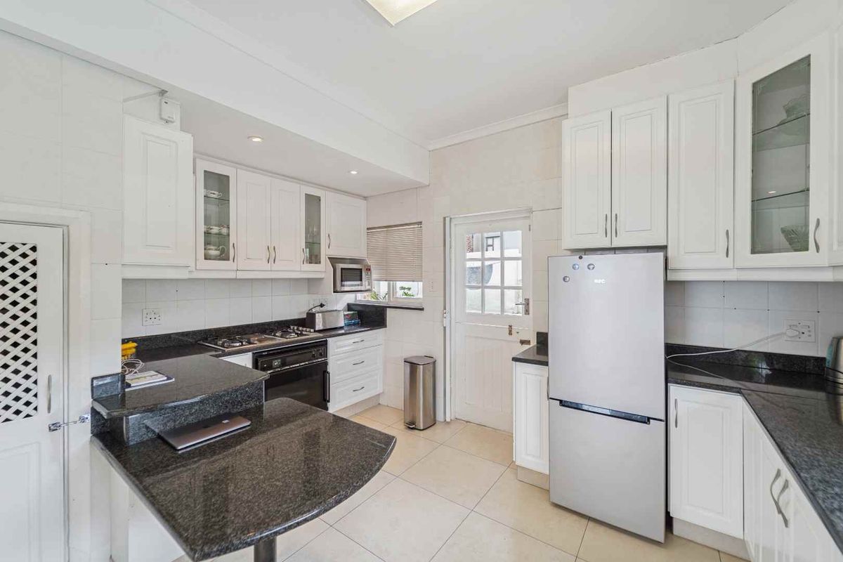 A functional kitchen featuring white cabinetry, dark granite countertops, a built-in oven, gas hob, and tiled flooring with direct exterior access.