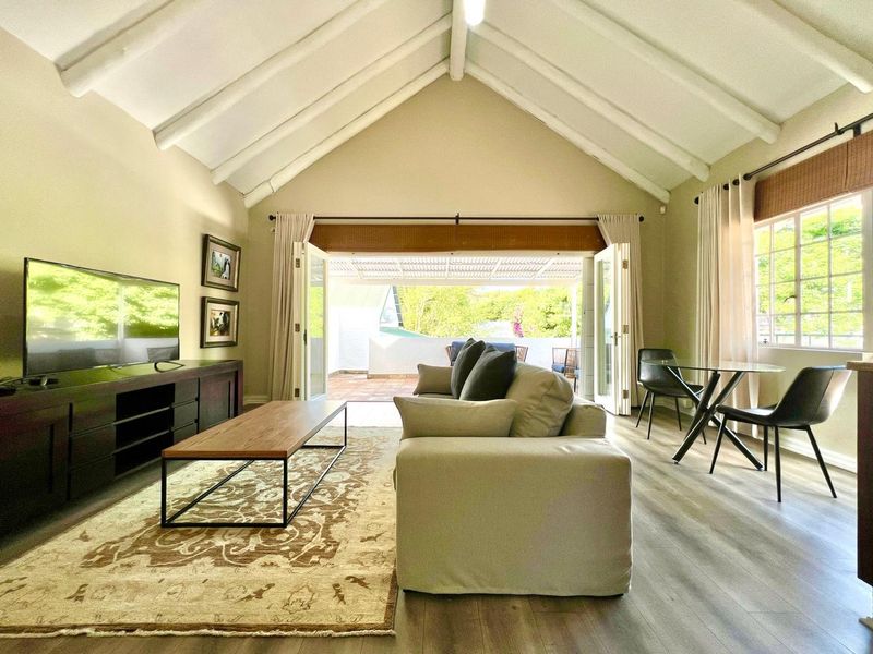 Spacious open-plan living area featuring a high vaulted ceiling with exposed beams, laminate flooring, and seamless access to an outdoor patio through double doors.
