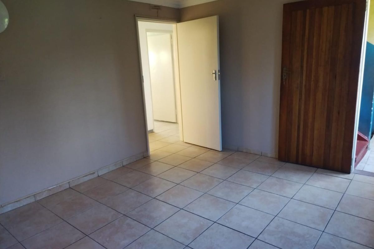 An empty living area featuring neutral wall paint, ceramic floor tiles, and a solid wooden door leading to an adjacent hallway.