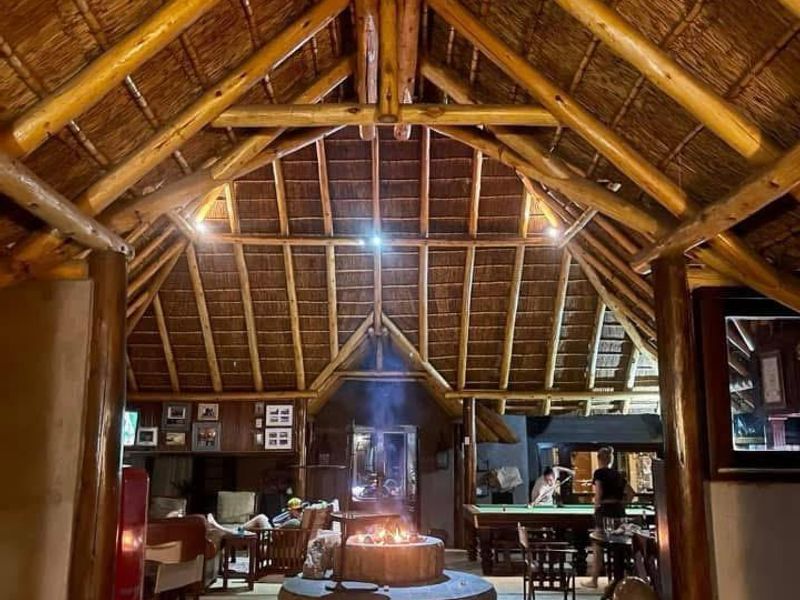 Spacious living area featuring a high vaulted thatched ceiling with exposed timber rafters and a central stone fireplace as a focal point.