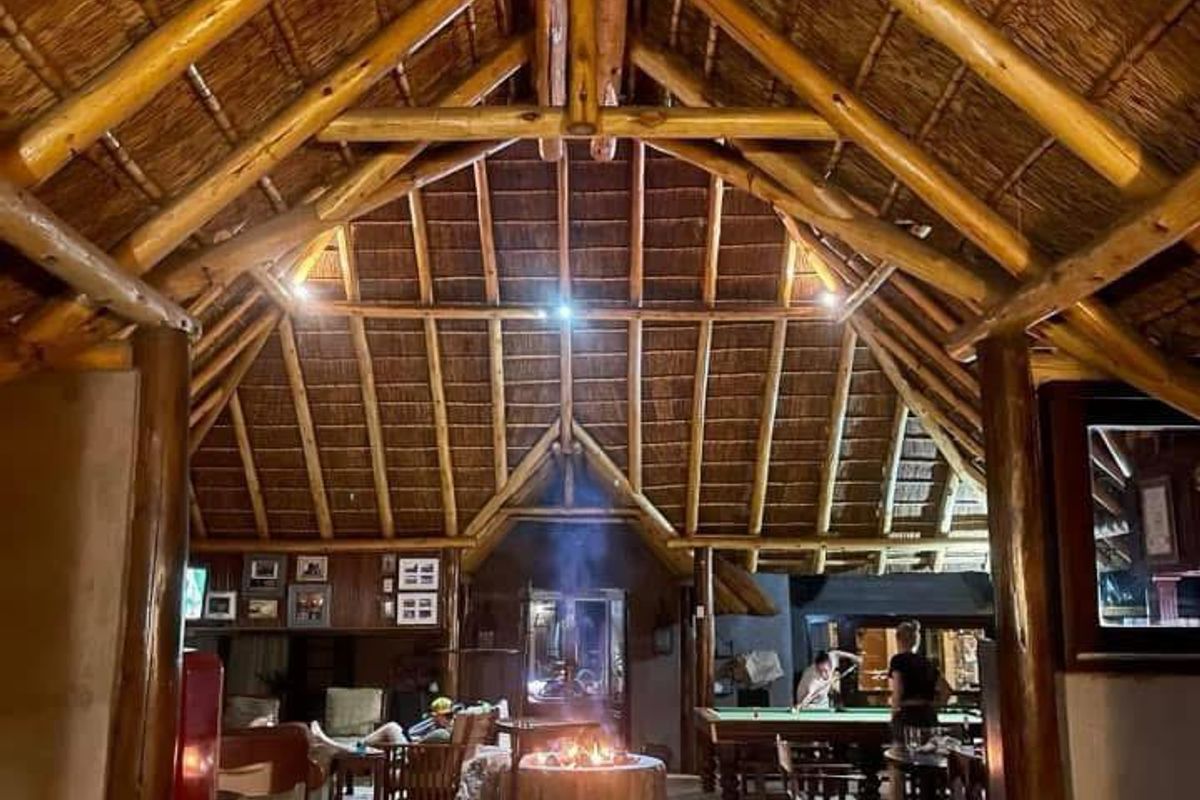 Spacious living area featuring a high vaulted thatched ceiling with exposed timber rafters and a central stone fireplace as a focal point.