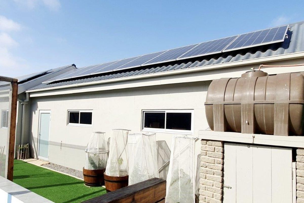 Rear exterior view featuring solar panels on the roof, a water storage tank, and a paved pool area with artificial lawn.