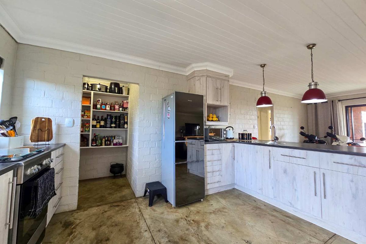 Open-plan kitchen featuring light wood-grain cabinetry, a built-in pantry nook, and a breakfast counter with pendant lighting.