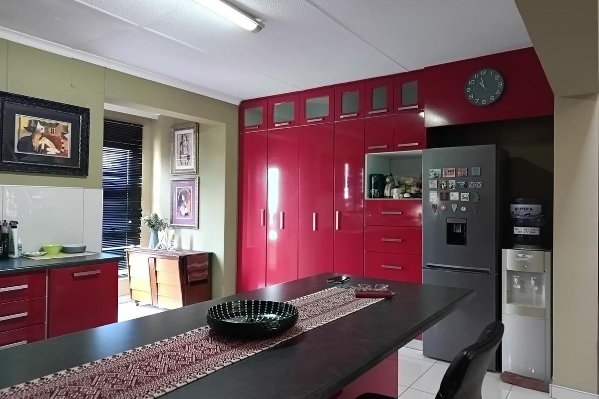A kitchen featuring high-gloss red cabinetry, a central island, and tiled flooring, offering ample storage space and a functional layout.