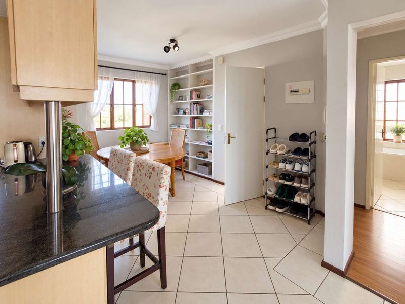Open-plan living and dining area featuring ceramic floor tiles, built-in shelving, and a granite-topped kitchen breakfast bar with views into the adjacent bathroom.