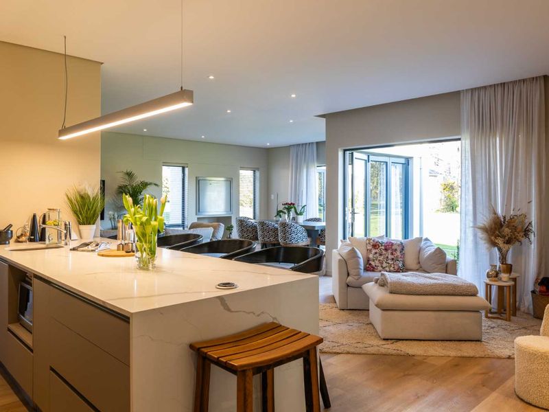Modern open-plan living area featuring a sleek kitchen island with stone countertops, recessed lighting, and seamless flow to the outdoor patio through bi-fold doors.