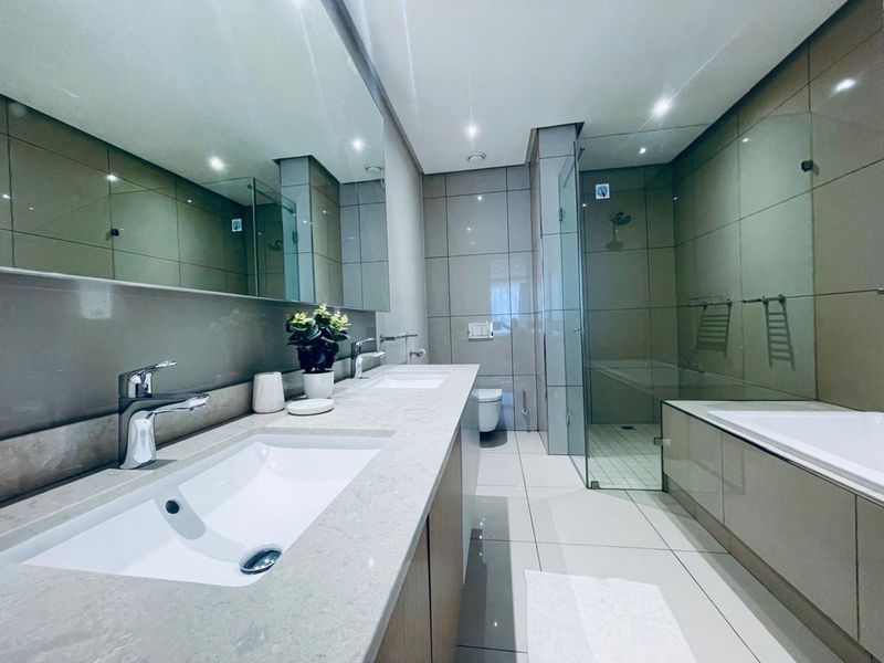 Modern bathroom featuring a double vanity with stone countertop, large wall mirror, glass-enclosed shower, and a built-in bathtub with neutral tiled finishes.