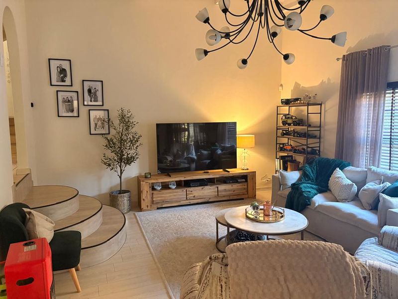 A cozy living room featuring a unique raised platform area, modern laminate flooring, and a statement chandelier, creating a warm and inviting atmosphere.