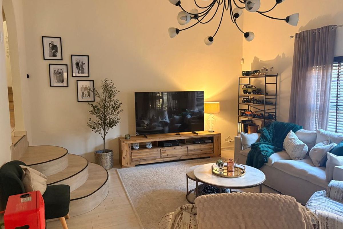A cozy living room featuring a unique raised platform area, modern laminate flooring, and a statement chandelier, creating a warm and inviting atmosphere.