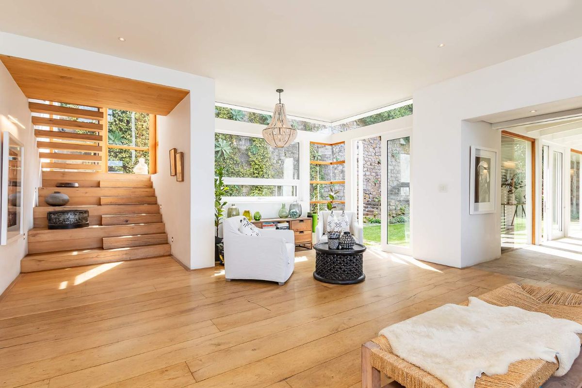 Bright and spacious living area featuring high-quality timber flooring, a striking floating timber staircase, and large windows overlooking a landscaped garden.