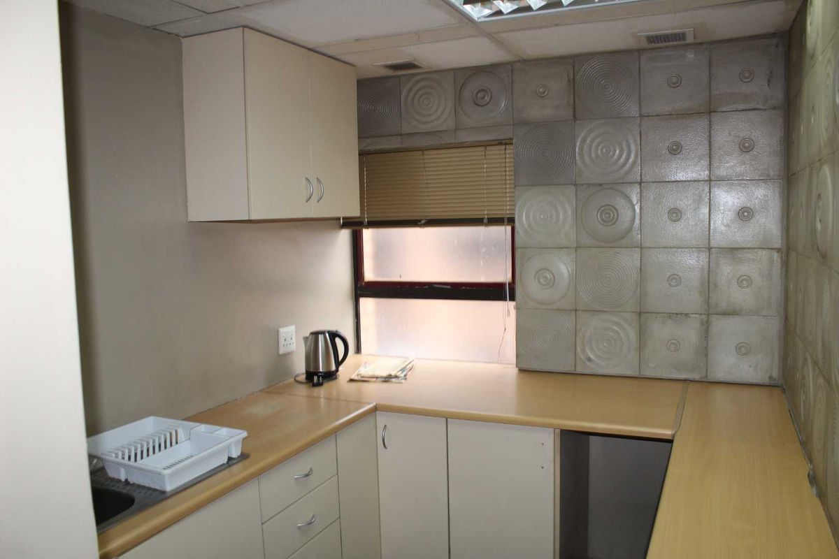 A compact office kitchenette featuring laminate countertops, built-in cabinetry, and textured decorative wall tiles.