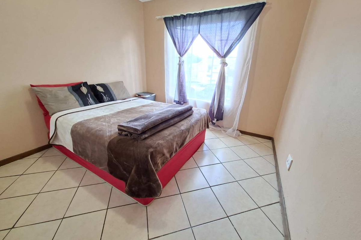 A bedroom featuring tiled flooring and a window with a curtain rod. Visible water staining on the ceiling suggests potential maintenance requirements.