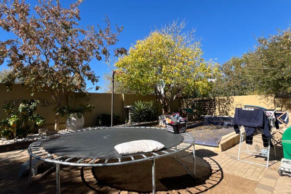 A private rear garden area featuring paved sections, established trees, and perimeter boundary walls, offering a functional outdoor space for recreation.
