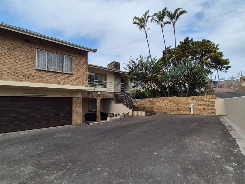 Front exterior view of a multi-level brick house featuring a double garage, paved driveway, and an elevated balcony with external staircase access.