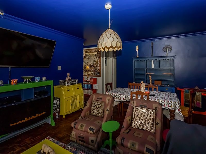 A living room featuring dark blue walls, parquet flooring, and a built-in electric fireplace, offering a unique and bold interior aesthetic.