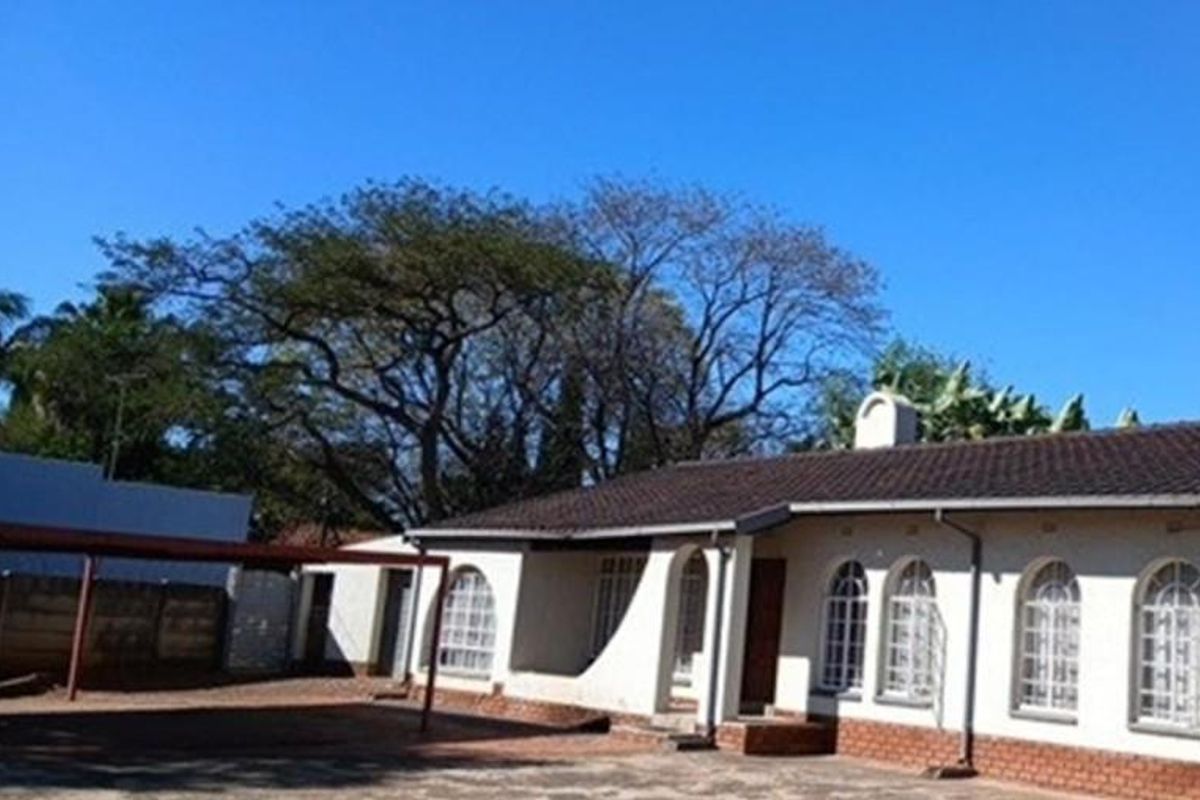 Front exterior view of a single-story residence featuring arched windows, a tiled roof, and an attached carport area.