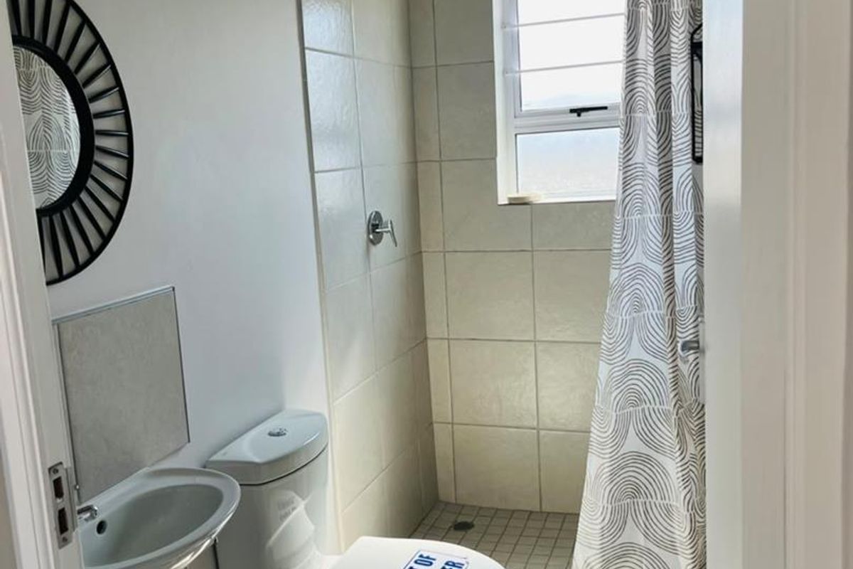 Compact bathroom featuring a shower, toilet, and wall-mounted basin with tiled finishes and exposed industrial-style ducting.