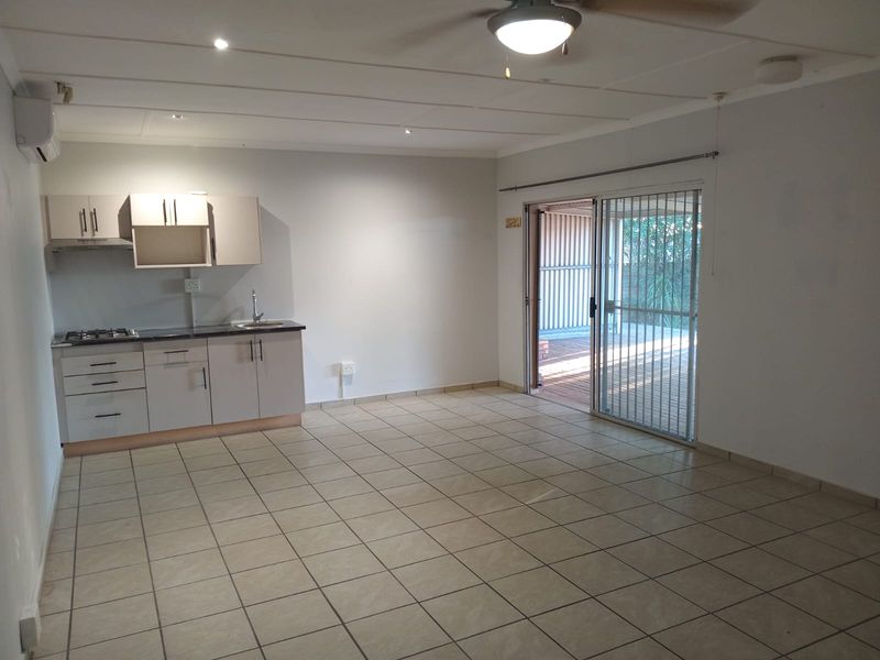 An open-plan living area featuring tiled floors, a compact kitchenette with built-in cabinetry and gas hob, and sliding doors leading to an outdoor space.