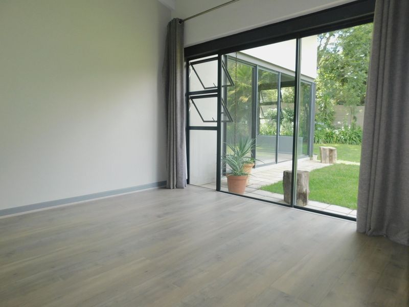 Bright and spacious living area featuring modern laminate flooring and large sliding glass doors that provide seamless access to the garden.