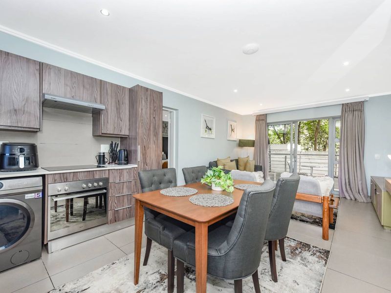 Modern open-plan living area featuring a well-equipped kitchen with built-in appliances, tiled flooring, and sliding glass doors leading to an outdoor space.
