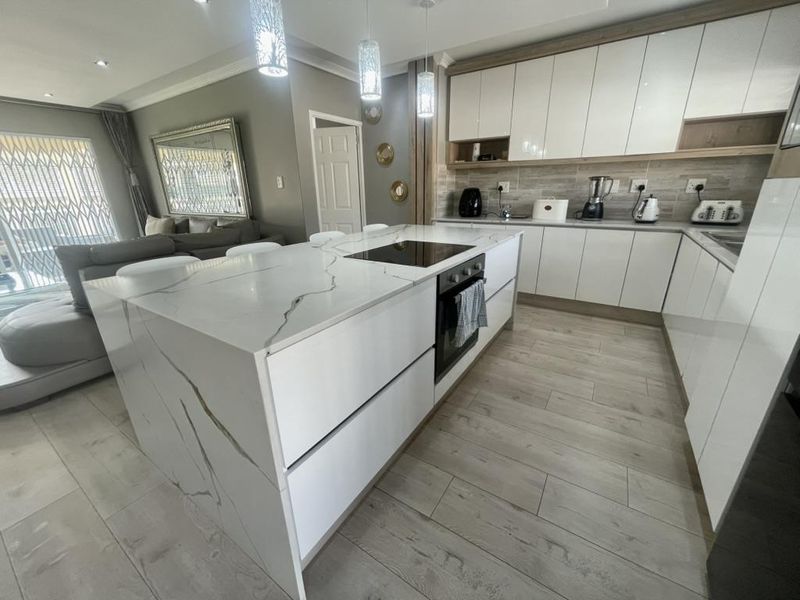 Modern open-plan kitchen featuring a large quartz-topped island, sleek gloss cabinetry, integrated appliances, and contemporary pendant lighting, seamlessly flowing into the living area.