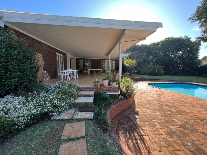 Spacious covered patio overlooking a swimming pool and landscaped garden, featuring brick paving and tiled flooring.