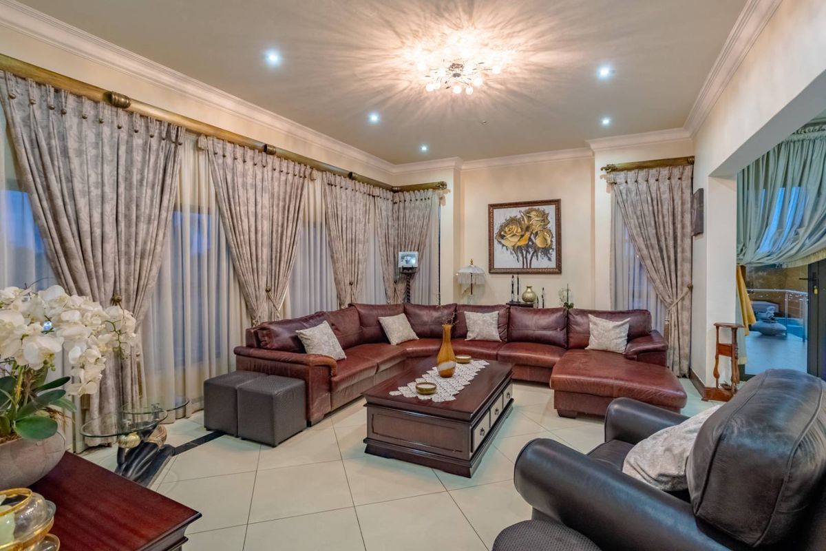 Spacious living room featuring tiled flooring, recessed downlighting, and large windows with elegant curtain treatments, creating a comfortable and well-lit atmosphere.