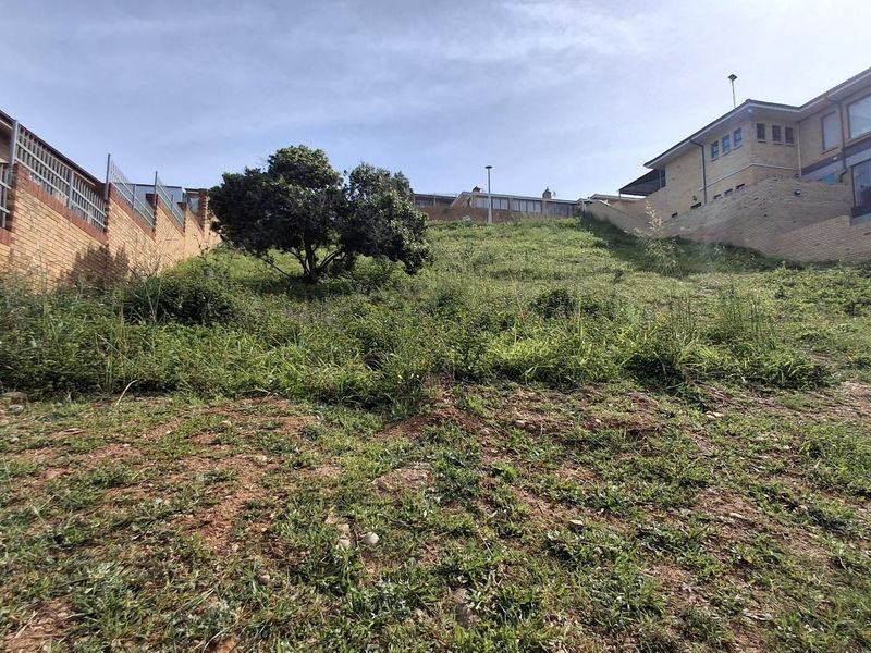 A sloped, undeveloped residential plot featuring established boundary retaining walls and surrounding residential properties.