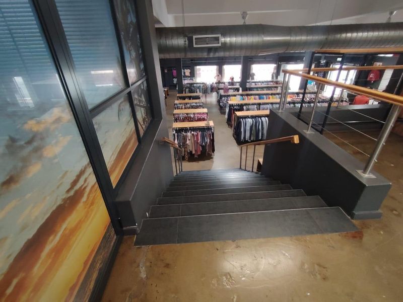 View looking down a staircase into an open-plan retail space featuring industrial exposed ducting and polished concrete floors.