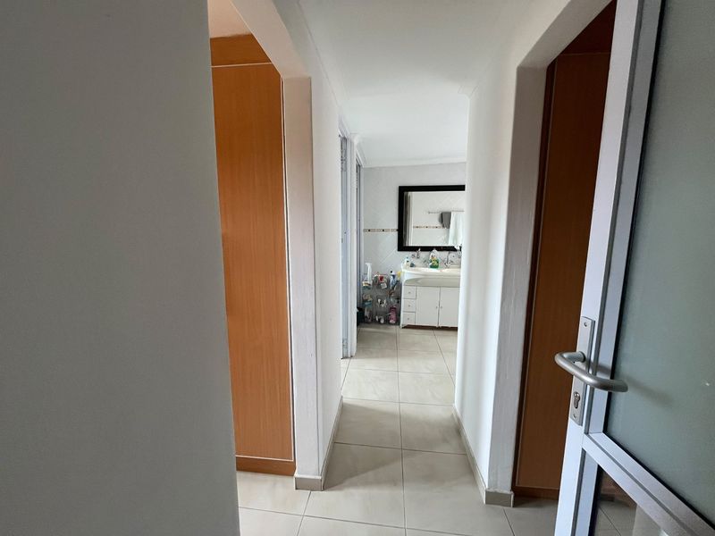 A bright hallway featuring tiled flooring and built-in cupboards, leading directly into a bathroom area with a vanity unit.