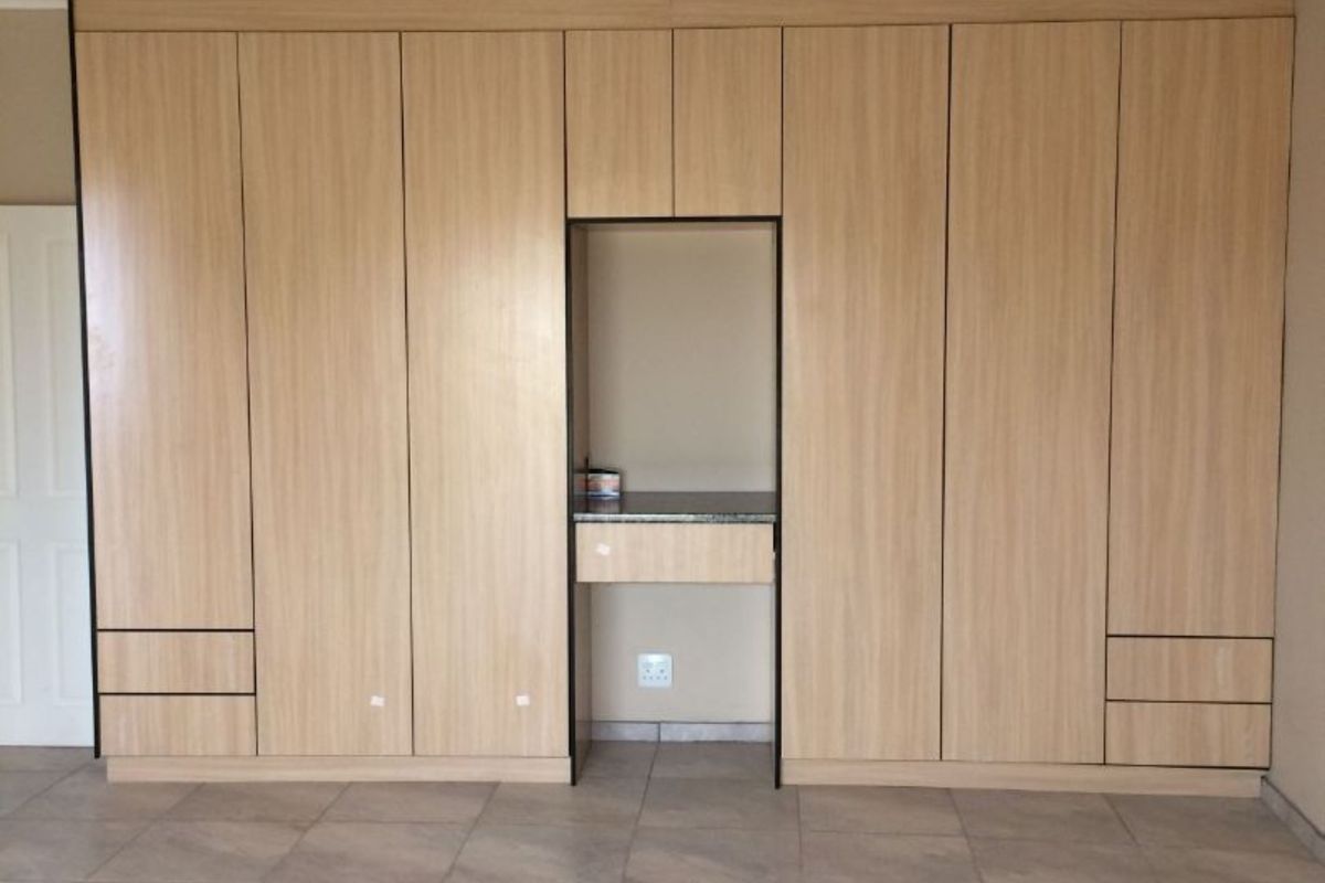 A spacious room featuring extensive built-in light wood cabinetry with integrated shelving and a central desk nook, complemented by tiled flooring and a ceiling fan.