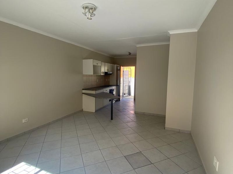 Open-plan living and kitchen area featuring tiled flooring, built-in cabinetry, a breakfast bar, and direct access to the exterior via a security gate.
