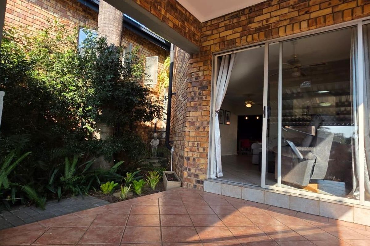 A covered patio area featuring face brick walls and tiled flooring, providing direct access to the interior living space through a sliding glass door.