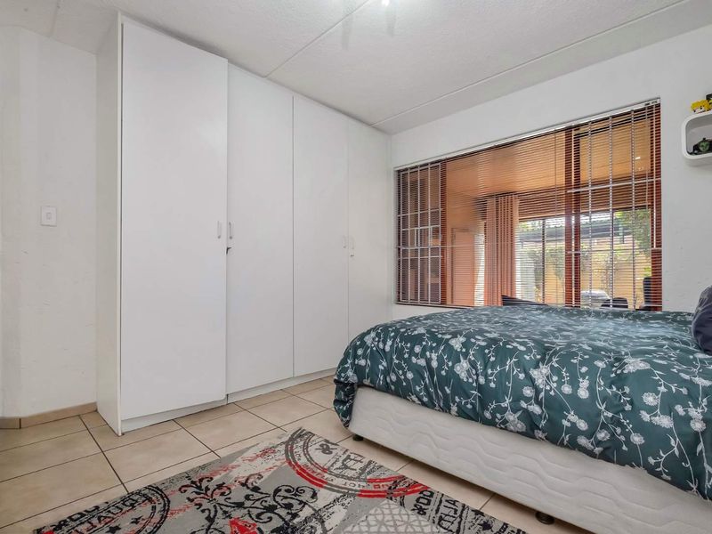 A bedroom featuring built-in cupboards, tiled flooring, and large windows with venetian blinds, offering a functional and well-lit living space.