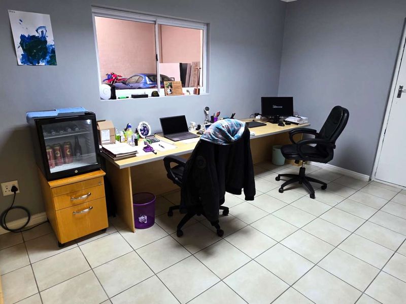 A functional office space featuring tiled flooring, a built-in desk, and an emergency exit door, suitable for professional or industrial administrative use.