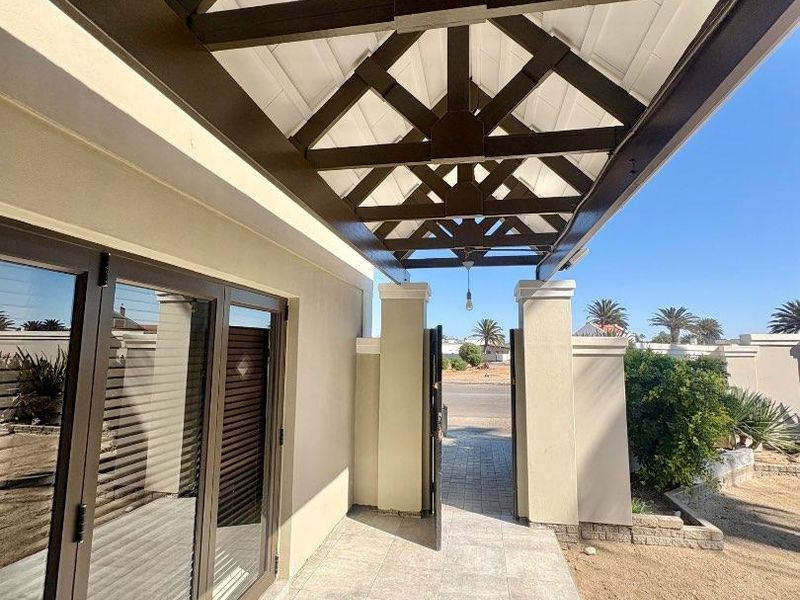 A covered outdoor patio area featuring a decorative timber pergola, tiled flooring, and modern aluminium sliding doors leading into the home.