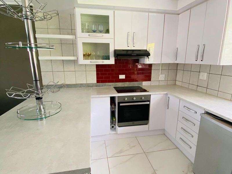 A modern kitchen featuring white cabinetry, stone-look countertops, a built-in oven with electric hob, and a striking red tiled backsplash.
