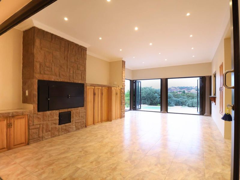 Spacious living area featuring a stone-clad built-in fireplace, custom cabinetry, and large stacking doors opening to an outdoor pool area.